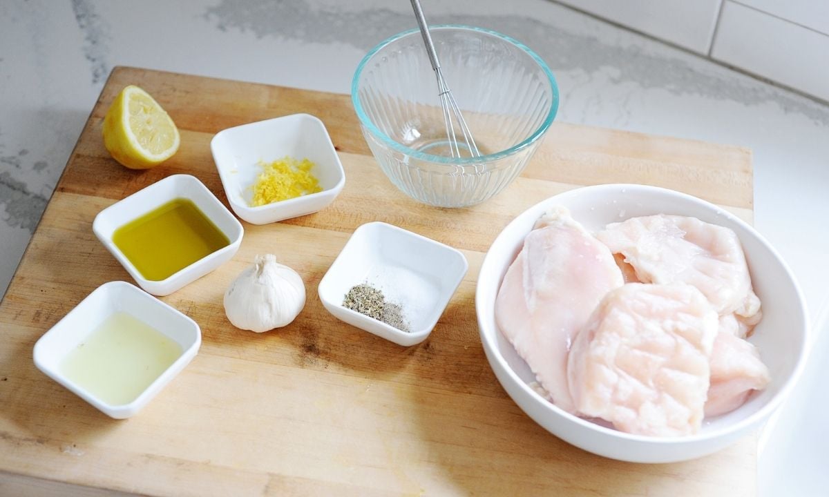 chicken breasts in a bowl with small dishes of seasonings on a cutting board