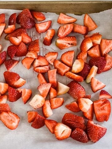 strawberries on sheet pan lined with parchment paper before freezing