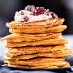 large stack of pumpkin pancakes topped with whipped cream and nuts