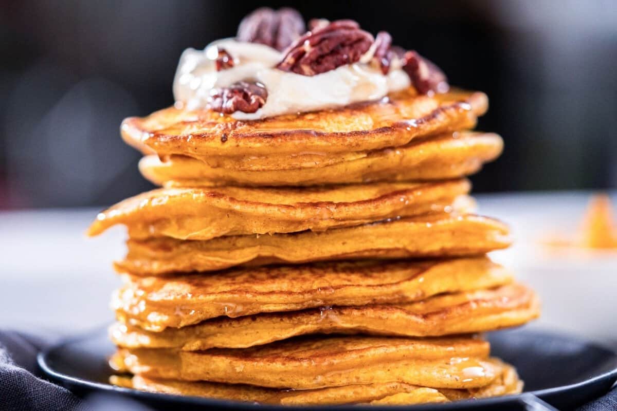 large stack of pumpkin pancakes topped with whipped cream and nuts