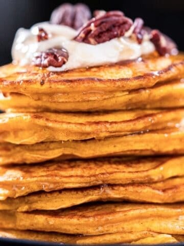 large stack of pumpkin pancakes topped with whipped cream and nuts