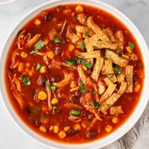 bowl filled with chicken tortilla soup (red tomato base, corn, black beans) topped with tortilla strips