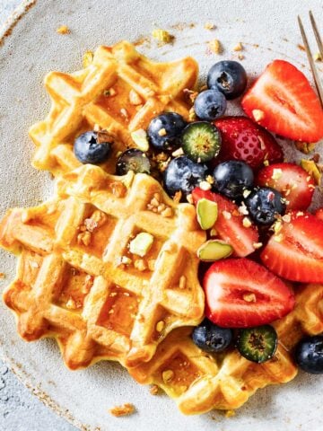 three waffles on a plate topped with fruit and granola