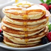 large stack of fluffy pancakes topped with butter and syrup
