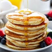 a fluffy stack of golden yeast pancakes on a plate topped with butter and syrup poured over the top and berries on the side