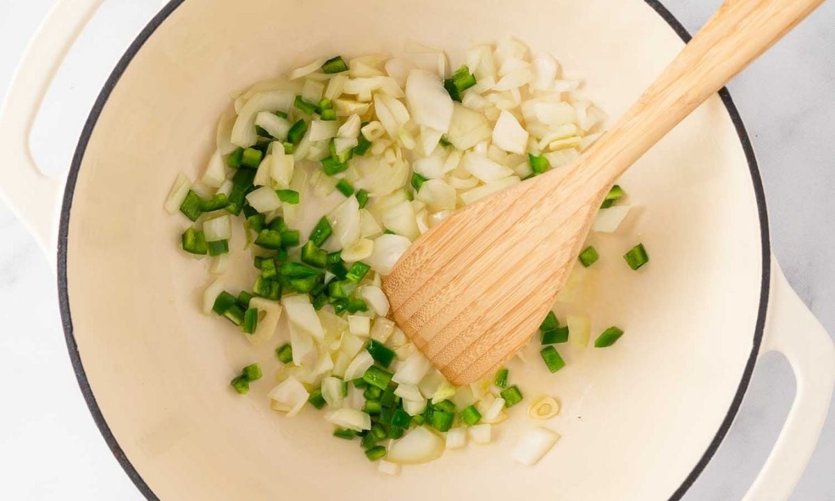 Diced onion, jalapeño, and garlic sautéing in olive oil in a Dutch oven with a wooden spoon.
