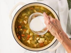 woman's hand adding slurry to a por with chicken potato stew