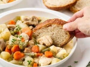dipping a slice of bread in a bowl of chicken potato stew