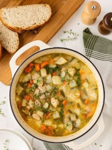 a pot with chicken potato stew surrounded by seasonings and slices of bread
