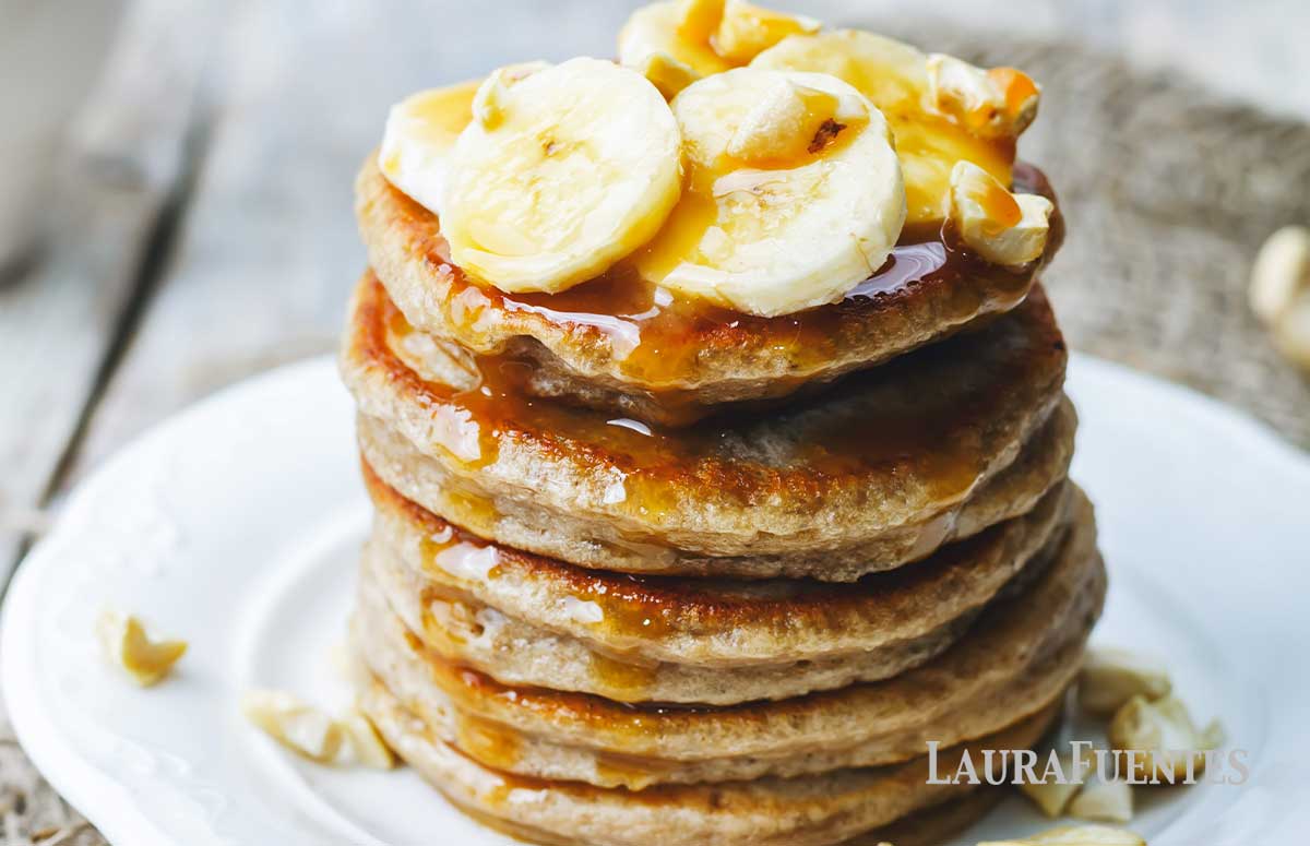 small stack of pancakes topped with bananas and nuts