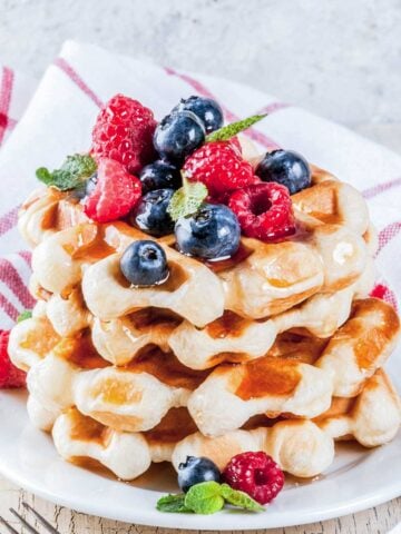 stack of waffles on a white plate topped with raspberries and blueberries