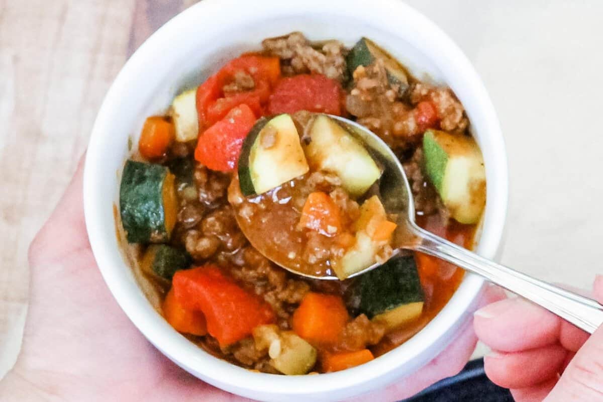 overhead view of a bowl of paleo chili and a hand holding a spoon