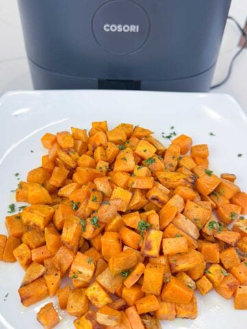 air fried sweet potatoes on a white plate in front of an air fryer