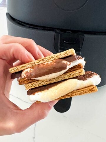 two smores stacked and held in front of an air fryer
