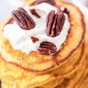 stack of pumpkin pancakes topped with whipped cream and pecans