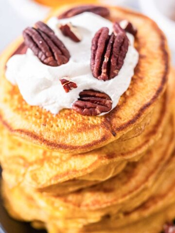 pumpkin pancakes topped with whipped cream and pecans