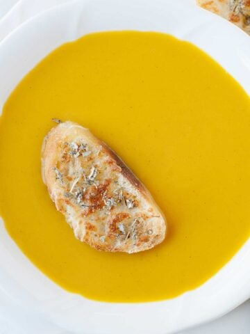 a bowl with butternut squash soup and a slice of toast on top
