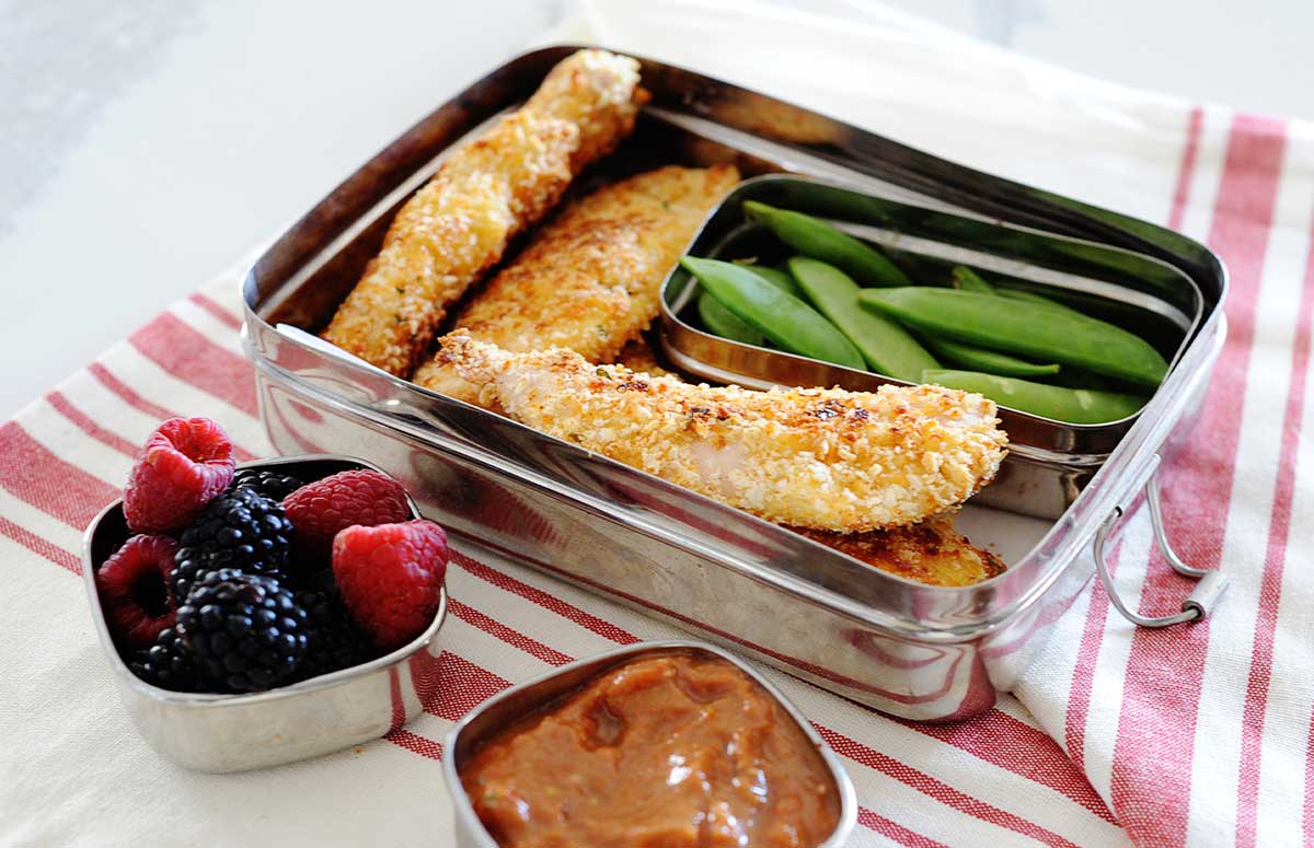 parmesan chicken tenders in a lunchbox with green peas, dipping sauce and berries