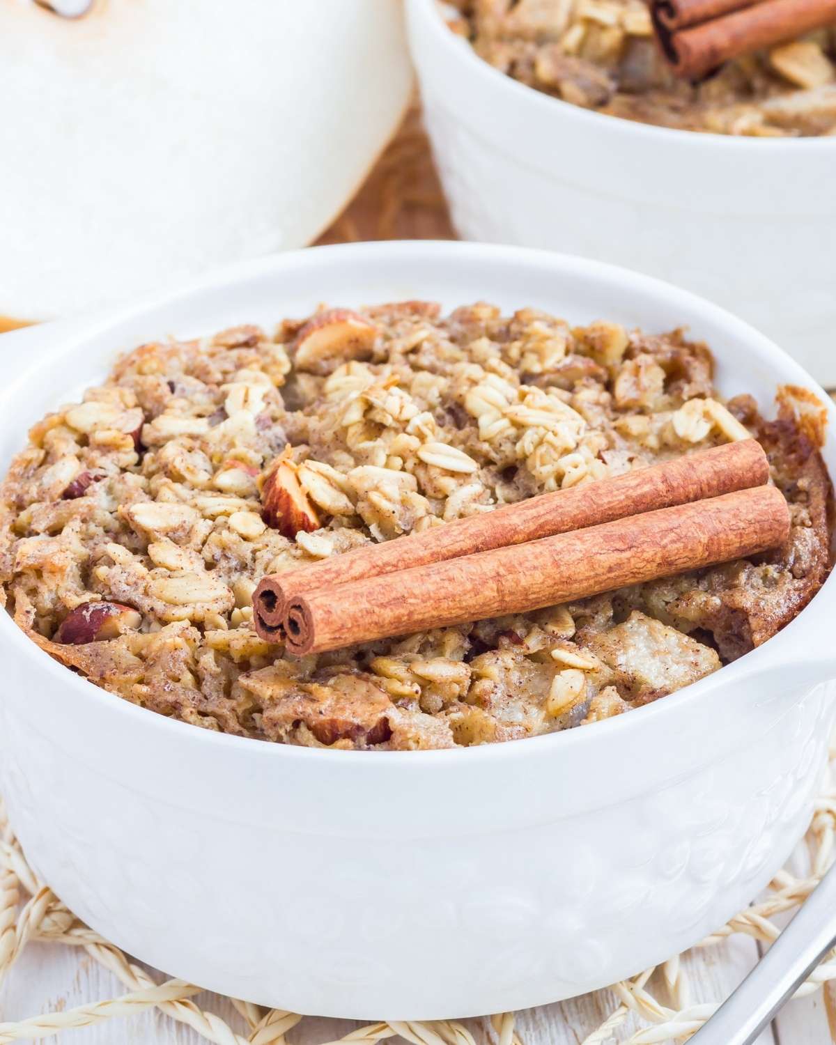 a bowl of pear baked oatmeal with two cinnamon sticks on top