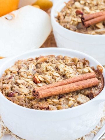 two bowls of pear baked oatmeal with two cinnamon sticks on top