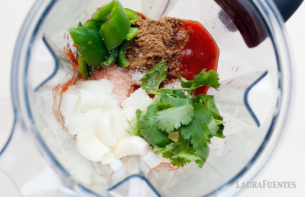 top view of a blender with jalapeño, cilantro, cumin, salt, tomato sauce and onion
