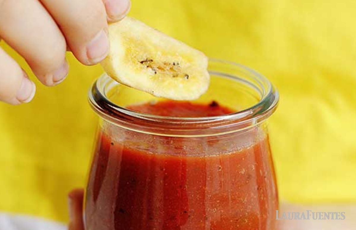 a kid dipping a banana chip on a jar of salsa