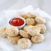 chicken nuggets on a plate with a small bowl of ketchup for dipping
