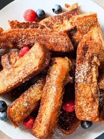 pile of French toast sticks on a plate with fresh berries
