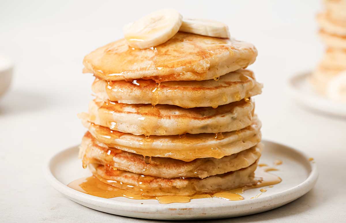 a stack of banana pancakes on a plate with sliced bananas on top and syrup