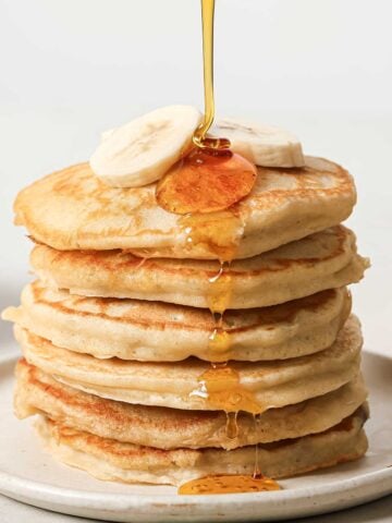 a stack of banana pancakes on a plate with sliced bananas on top and syrup being drizzled over them