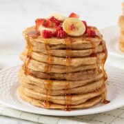 stack of pancakes made with cottage cheese and oats on a plate. they're topped with diced strawberries, bananas, and pancake syrup.