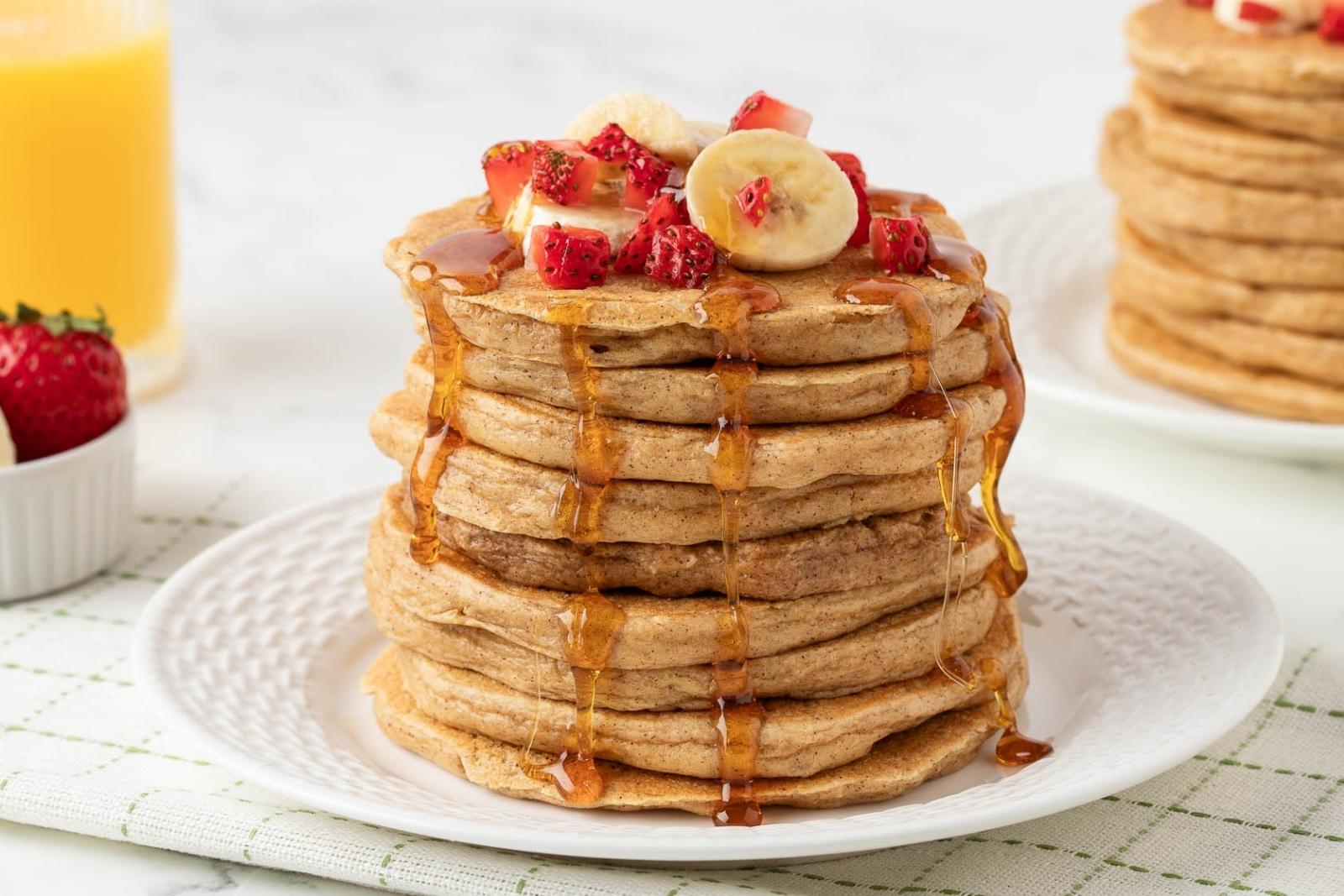 stack of pancakes made with cottage cheese and oats on a plate. they're topped with diced strawberries, bananas, and pancake syrup.