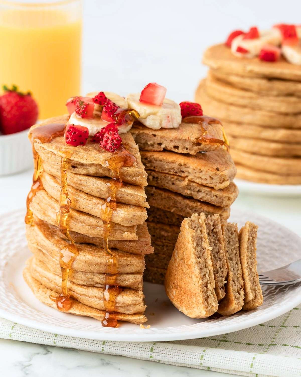 stack of cottage cheese oat pancakes on a plate, sliced to show their fluffy texture. they're topped with diced strawberries, bananas, and pancake syrup.