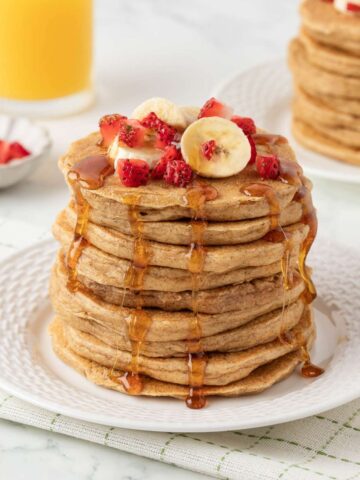 high protein cottage cheese oat pancakes on a plate topped with diced strawberries, bananas, and pancake syrup.