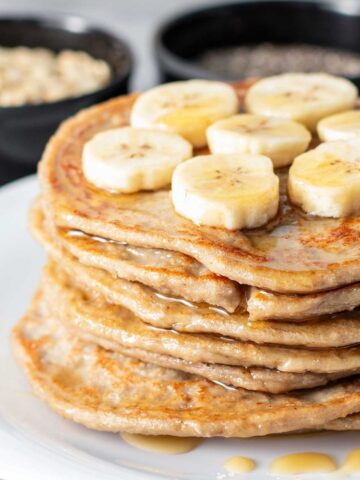 large stack of 3 ingredient oat pancakes topped with sliced bananas