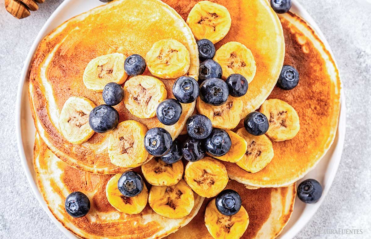 large stack of pancakes topped with blueberries and banana slices