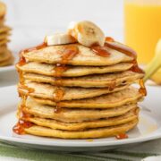 front view of 3 ingredient banana pancakes stacked on a plate topped with sliced bananas and syrup