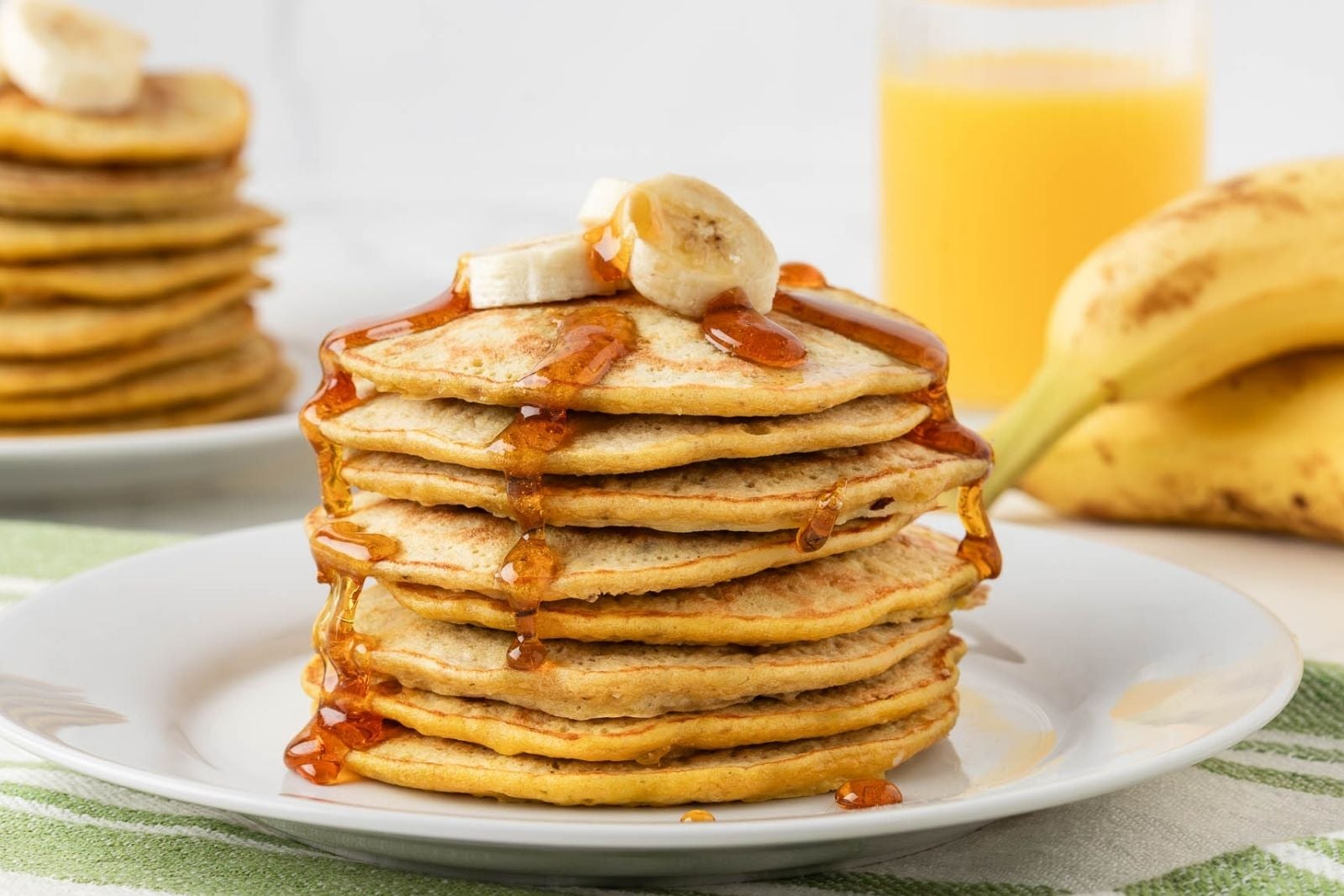 front view of 3 ingredient banana pancakes stacked on a plate topped with sliced bananas and syrup