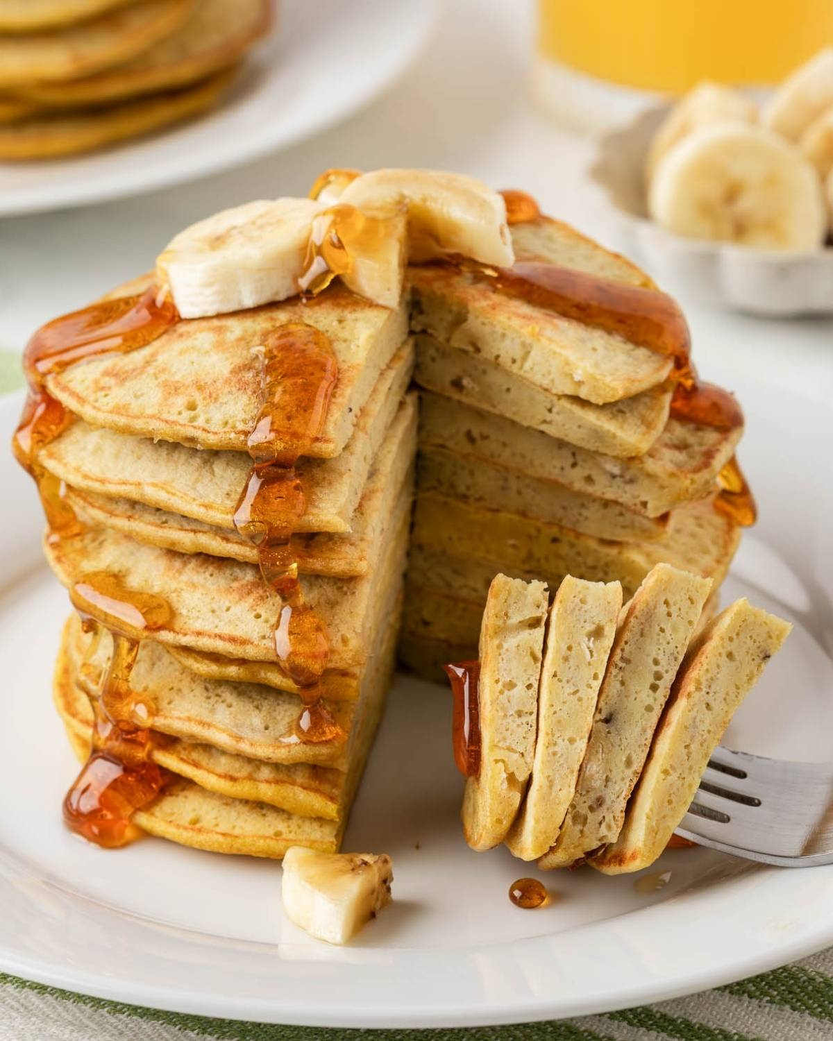 front view of 3 ingredient banana pancakes stacked on a plate topped with sliced bananas and syrup. the pancakes have been sliced to show their nice fluffy texture