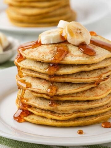 front view of 3 ingredient banana pancakes stacked on a plate topped with sliced bananas and syrup