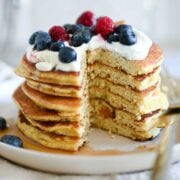 Stack of almond flour pancakes topped with cream and berries, with one bite cut out