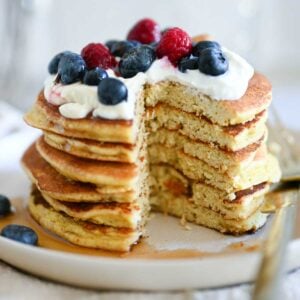 Stack of almond flour pancakes topped with cream and berries, with one bite cut out