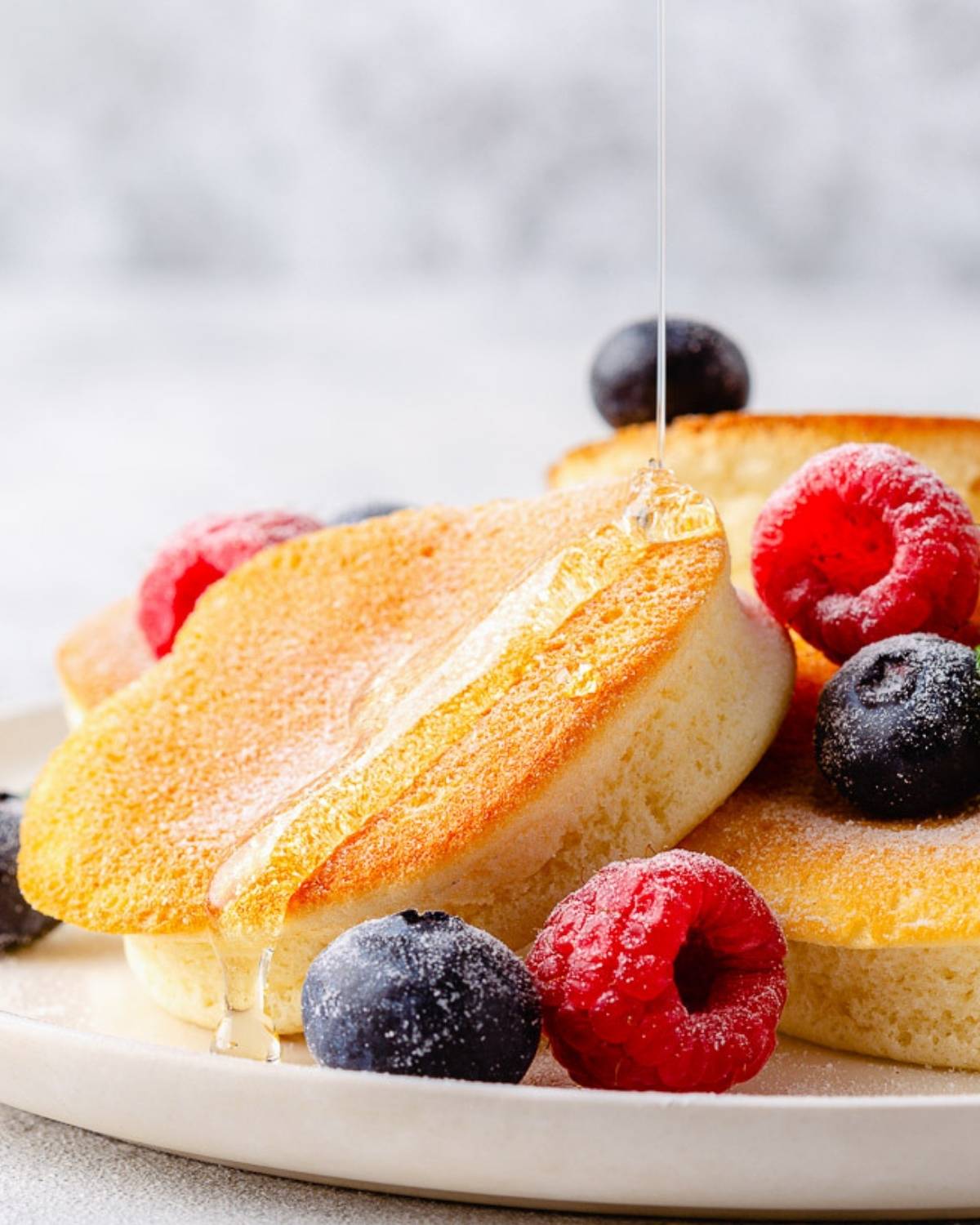 souffle pancakes on a plate with a drizzle of syrup with some blueberries and raspberries as topping