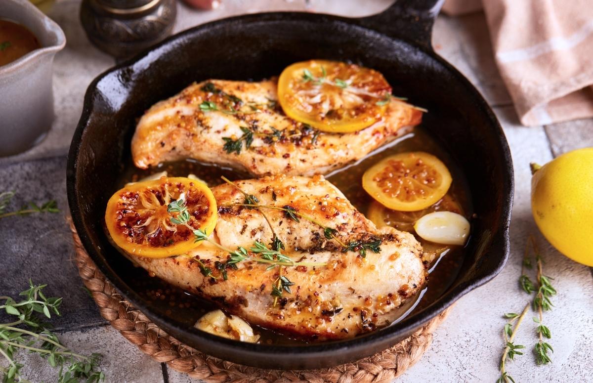 cooked chicken breasts in a pan with a few lemon slices and thyme on top