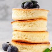 stack of souffle pancakes shown from the side on a plate with a few blueberries on top and on the plate