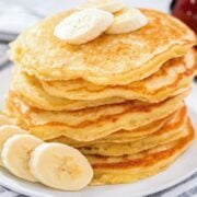 stack of pancakes topped with sliced bananas. More sliced bananas to the side