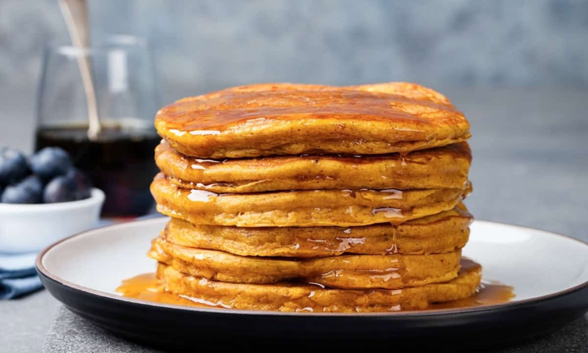 tall fluffy stack of pumpkin pancakes made with cottage cheese on a plate topped with pancake syrup