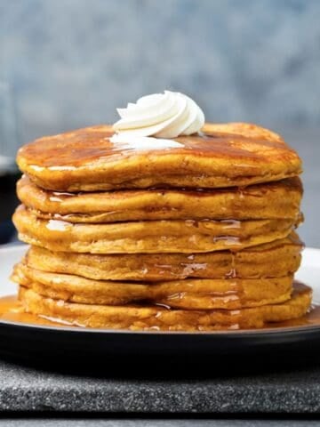 tall fluffy stack of pumpkin pancakes made with cottage cheese on a plate topped with a little whipped cream and pancake syrup