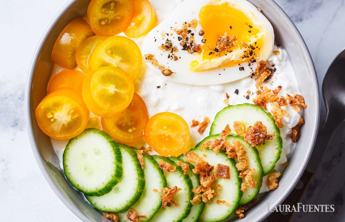 top view of a breakfast bowl with cottage cheese, cucumber, tomato, bacon and egg
