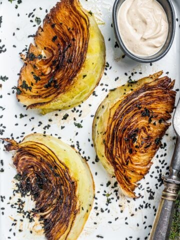 top view of three roasted cabbage quarters in a baking sheet and a little bowl with dressing